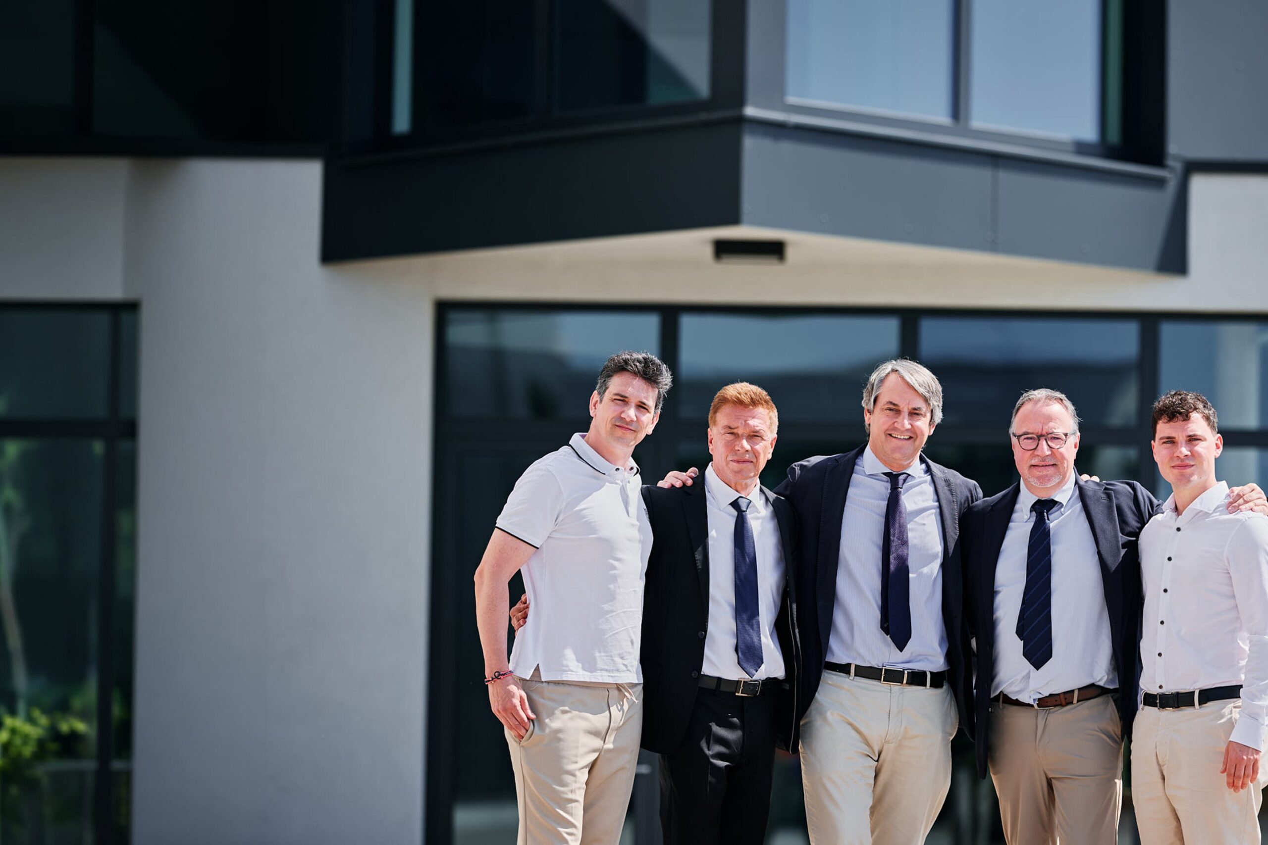 Zayer EMC Team mit Geschäftsleuten vor moderner Firmenfassade.